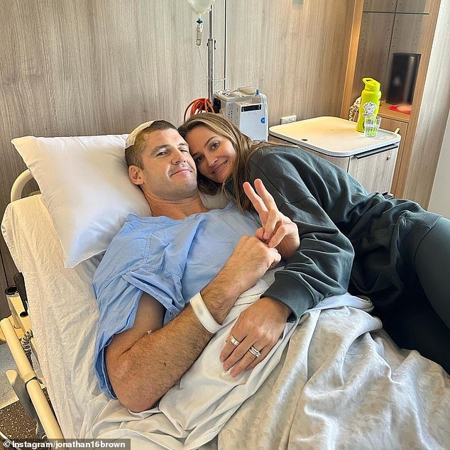 La leyenda del fútbol Jonathan Brown, de 44 años, es consolada por su esposa en el hospital después de una cirugía cerebral, mientras revela cómo se descubrió un tumor durante una exploración de rutina.